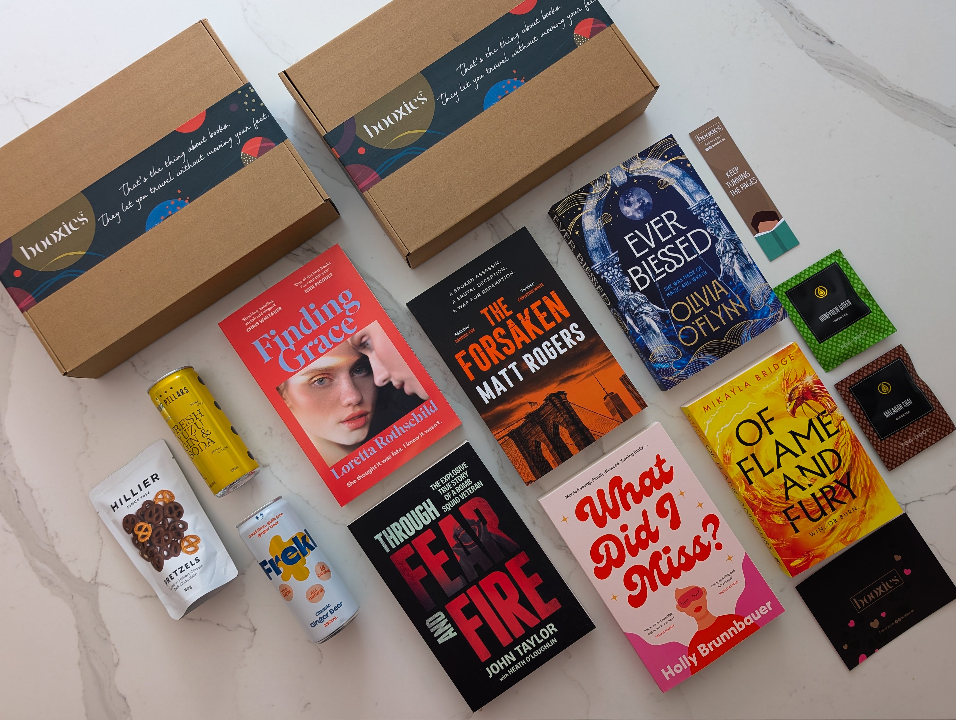 Collection of books and snacks on a white surface with two booxies boxes. this is August 2025 mystery booxies selection