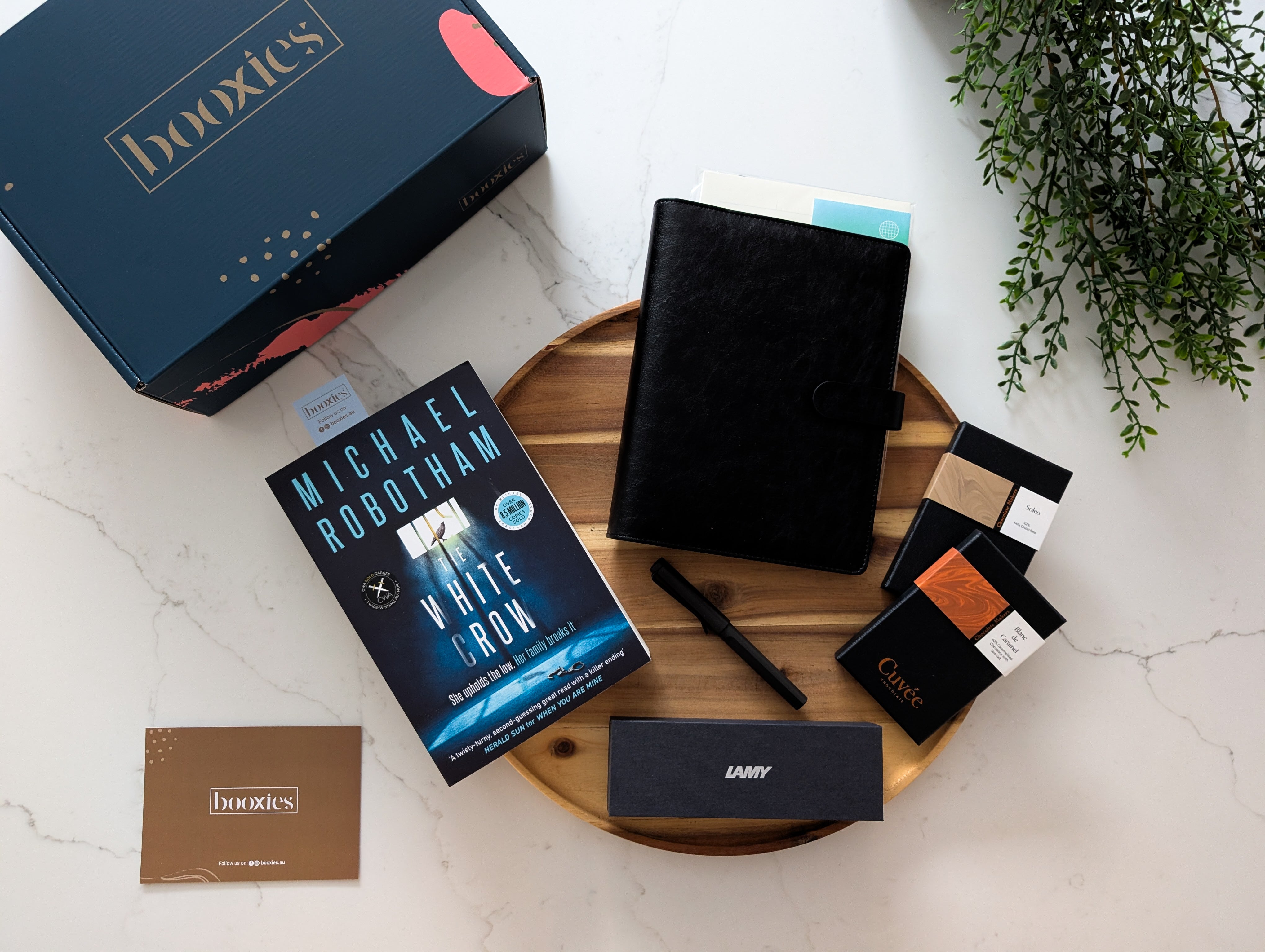 Collection of stationery items including books, notebooks, and a pen on a marble surface with a 'booxies' branded box.