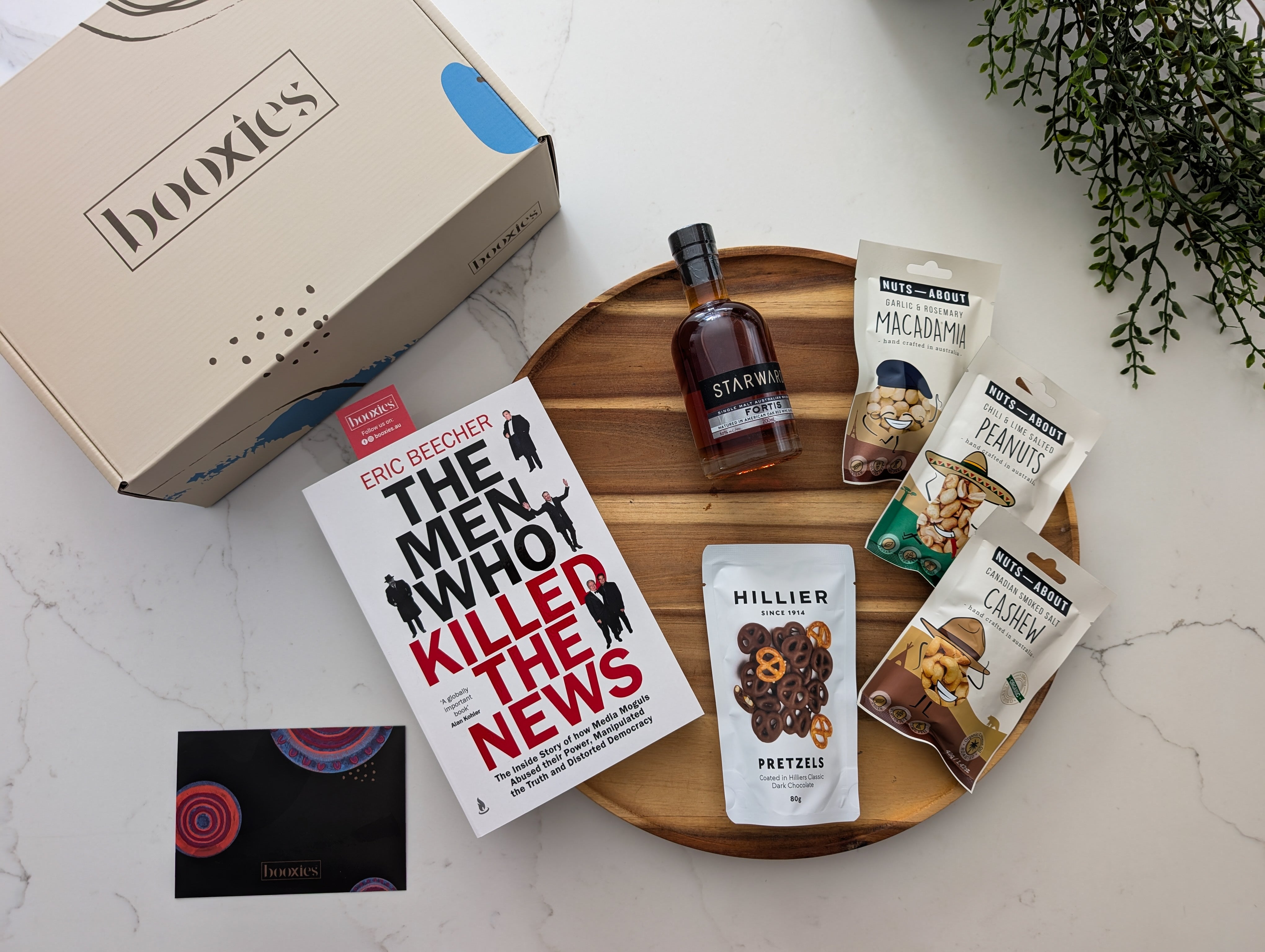 Gourmet gift set with book, alcohol, and snacks on a marble surface