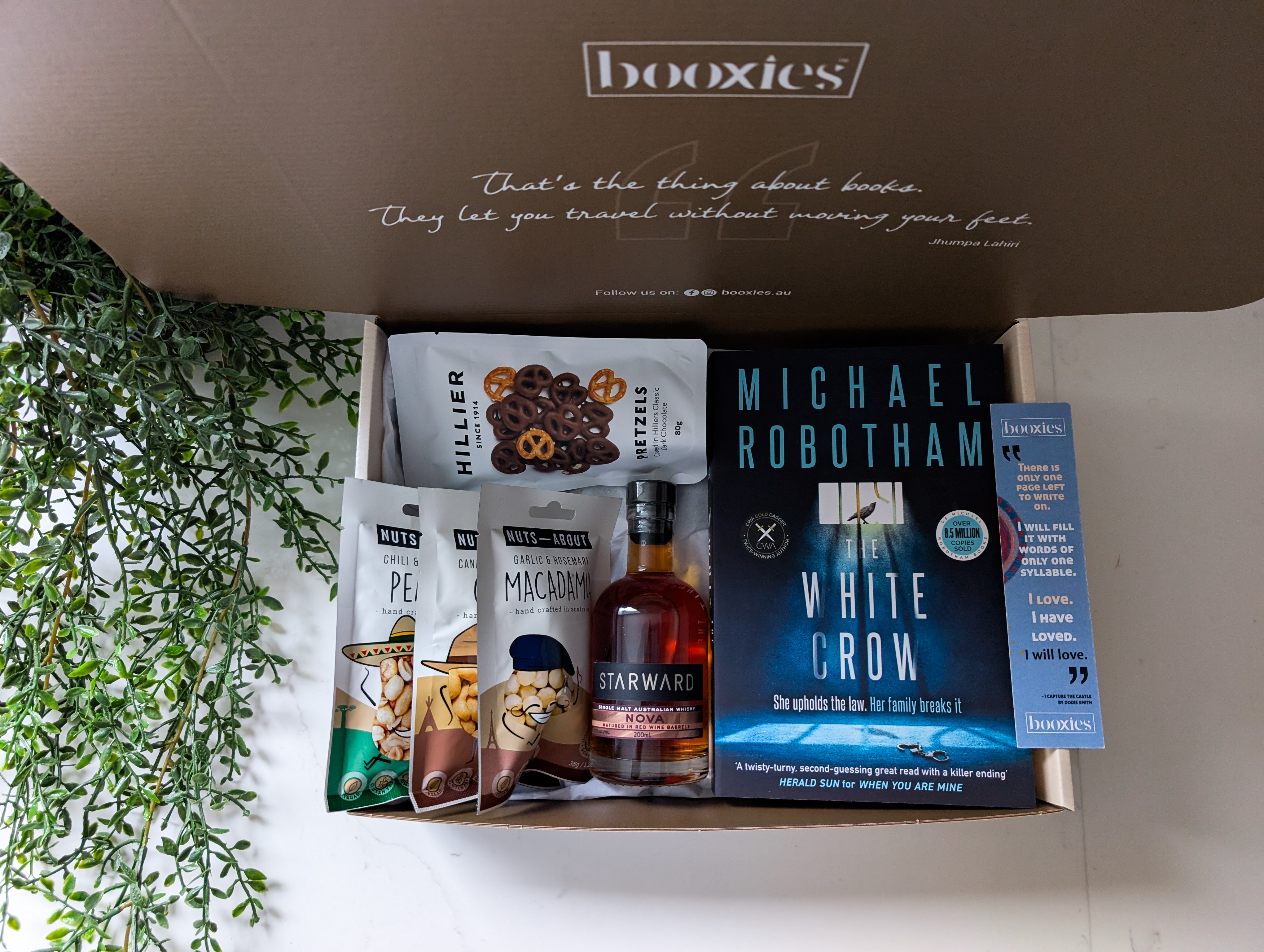Box from booxies with a book, snacks, and a bottle of whiskey on a white surface.