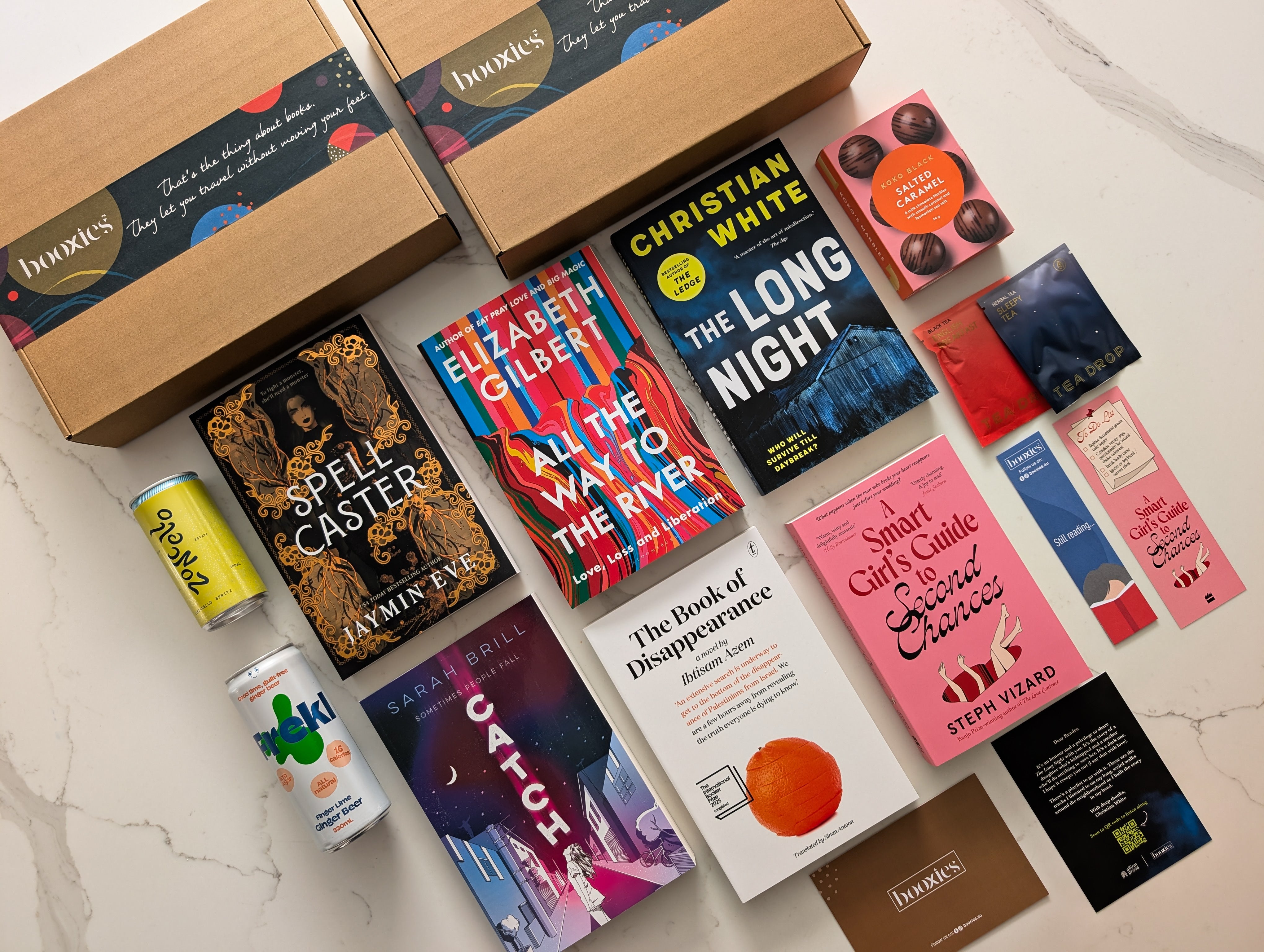 Collection of books and drinks on a marble surface showing the books and products of the month for Mystery Booxies.