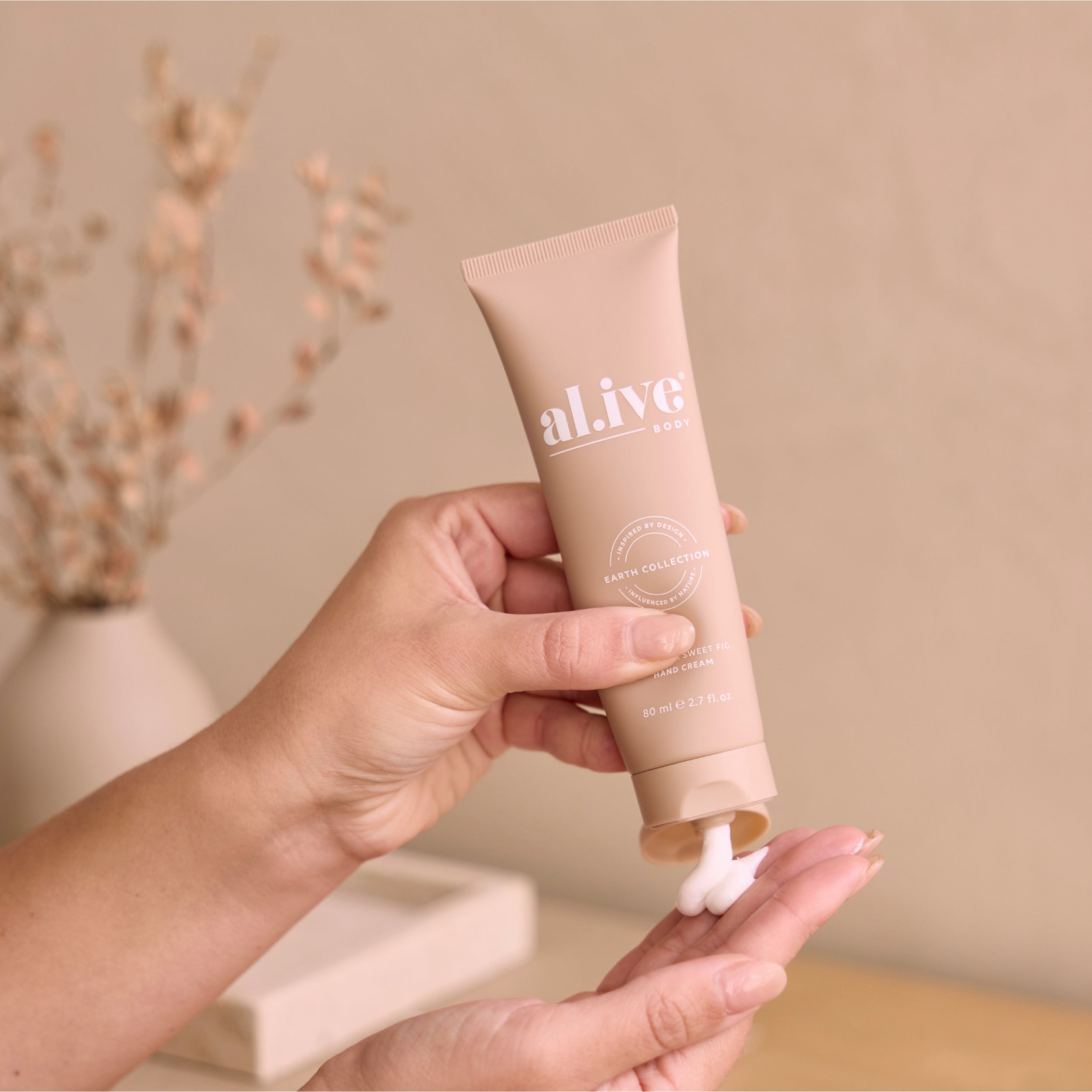 Hand holding a tube of 'al ive' cream against a neutral background