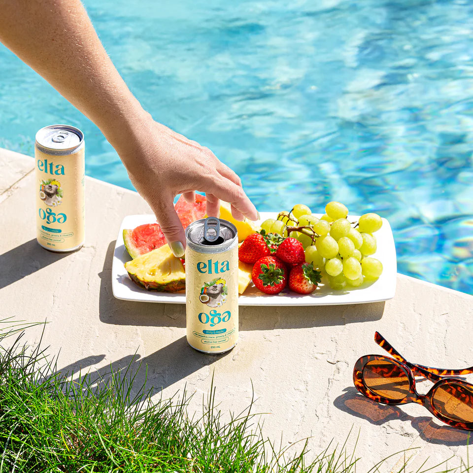 Hand reaching for a can of elta soda next to a plate of fruit by a pool.