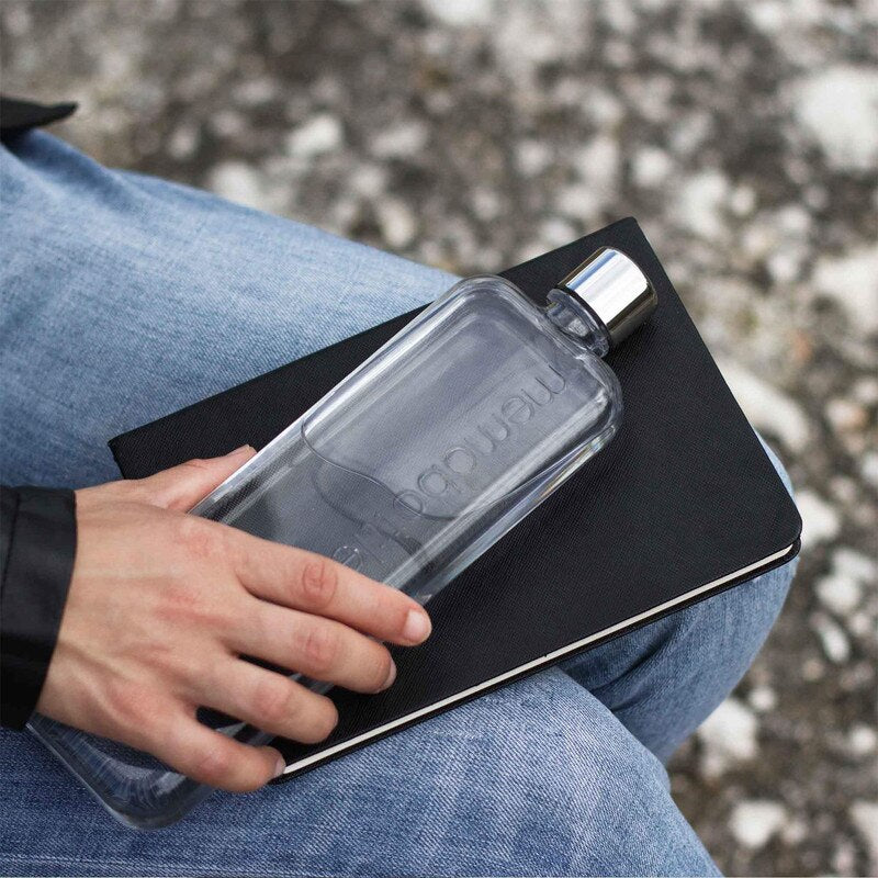 Person holding a transparent memobottle with a black cap on a notebook outdoors.