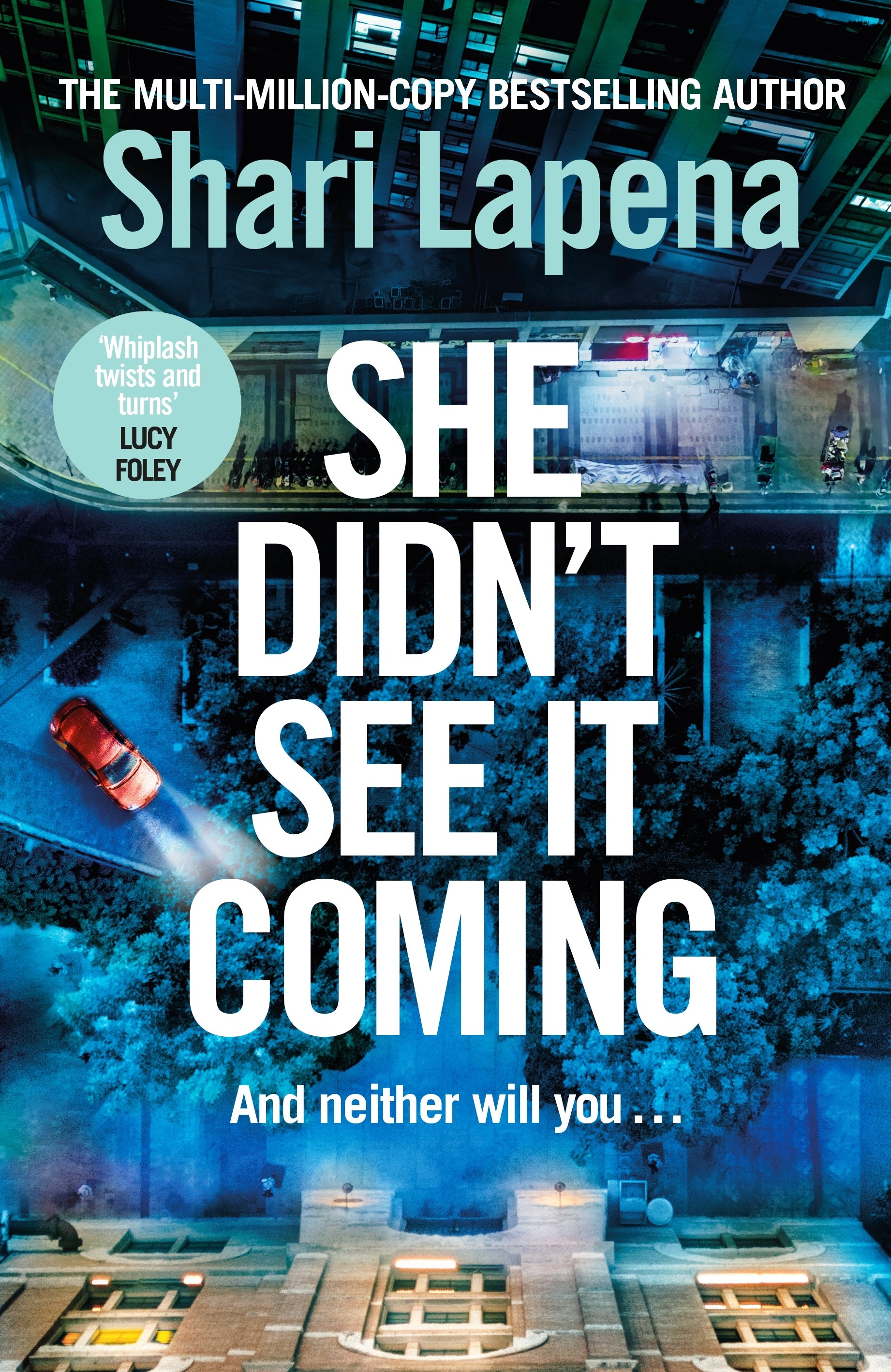 Book cover of 'She Didn't See It Coming' by Shari Lapena with a cityscape background.