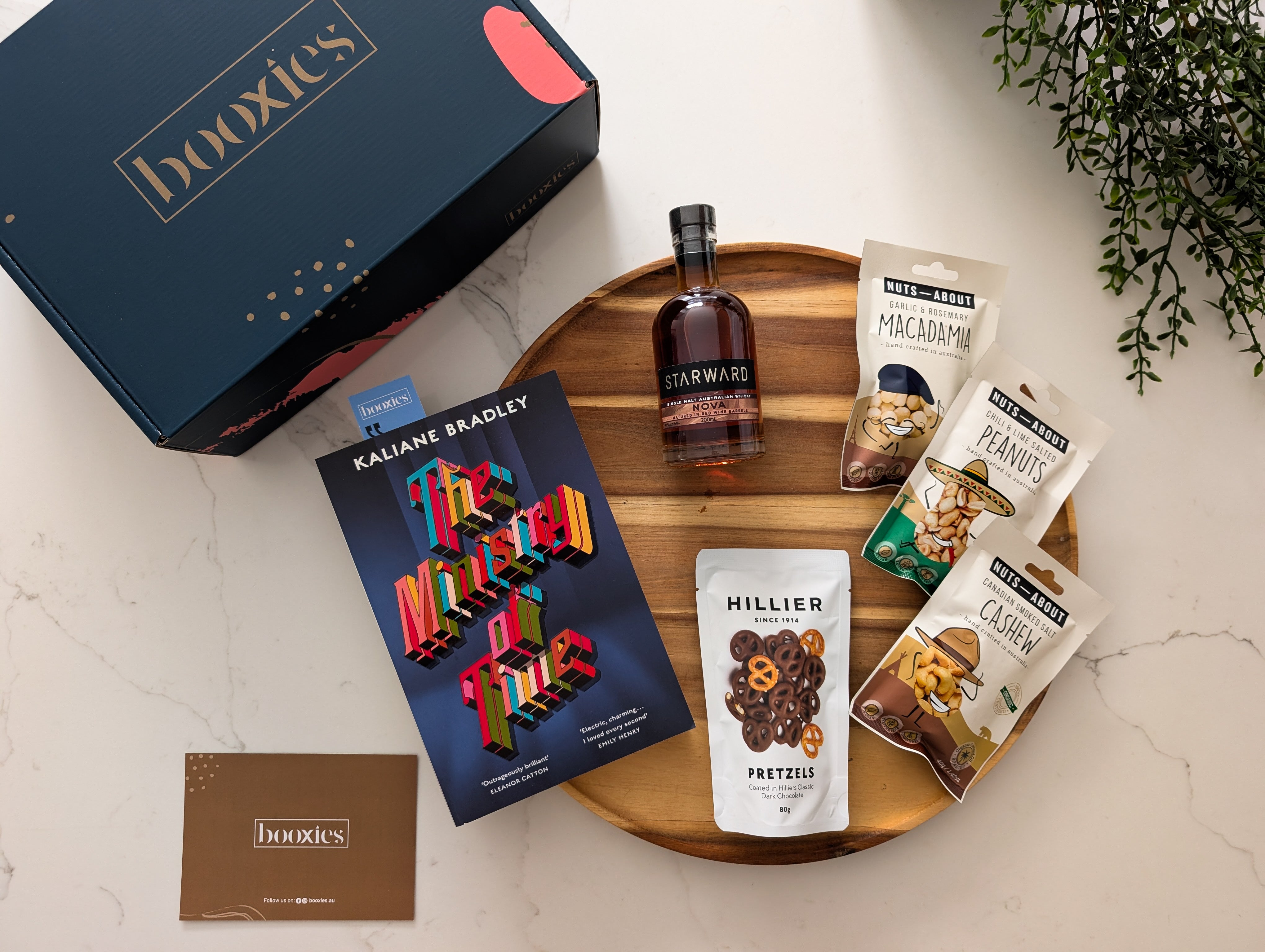 Gourmet gift set with chocolate bars, a bottle of whiskey, and snack packages on a marble surface.