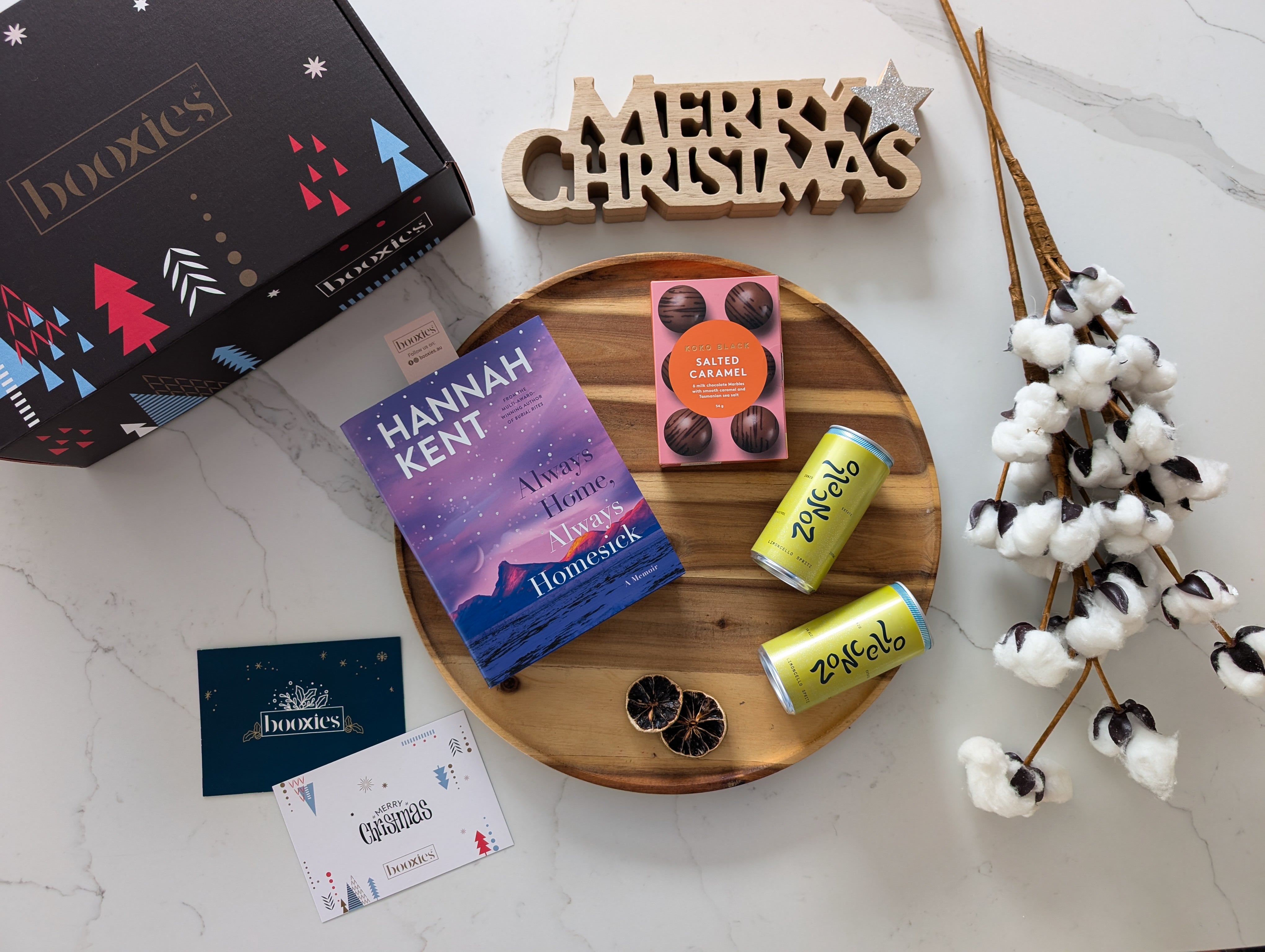 Limoncello & LIterature christmas booxies gift box showing 2x zoncello cans and a koko black marble chocolate with a selected book on a white marble background