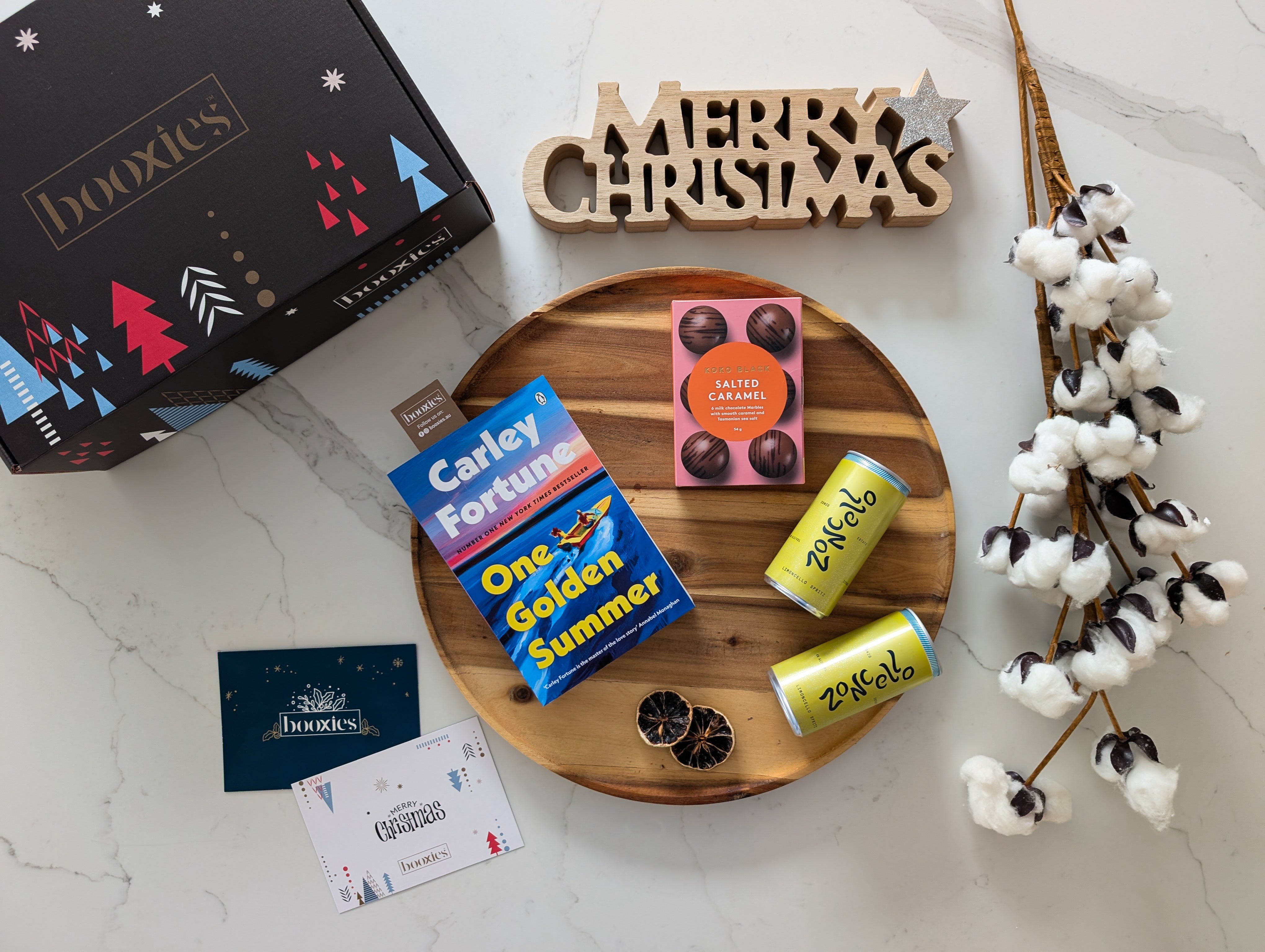 Wooden tray with books, a 'Merry Christmas' sign, and decorative items on a marble surface.