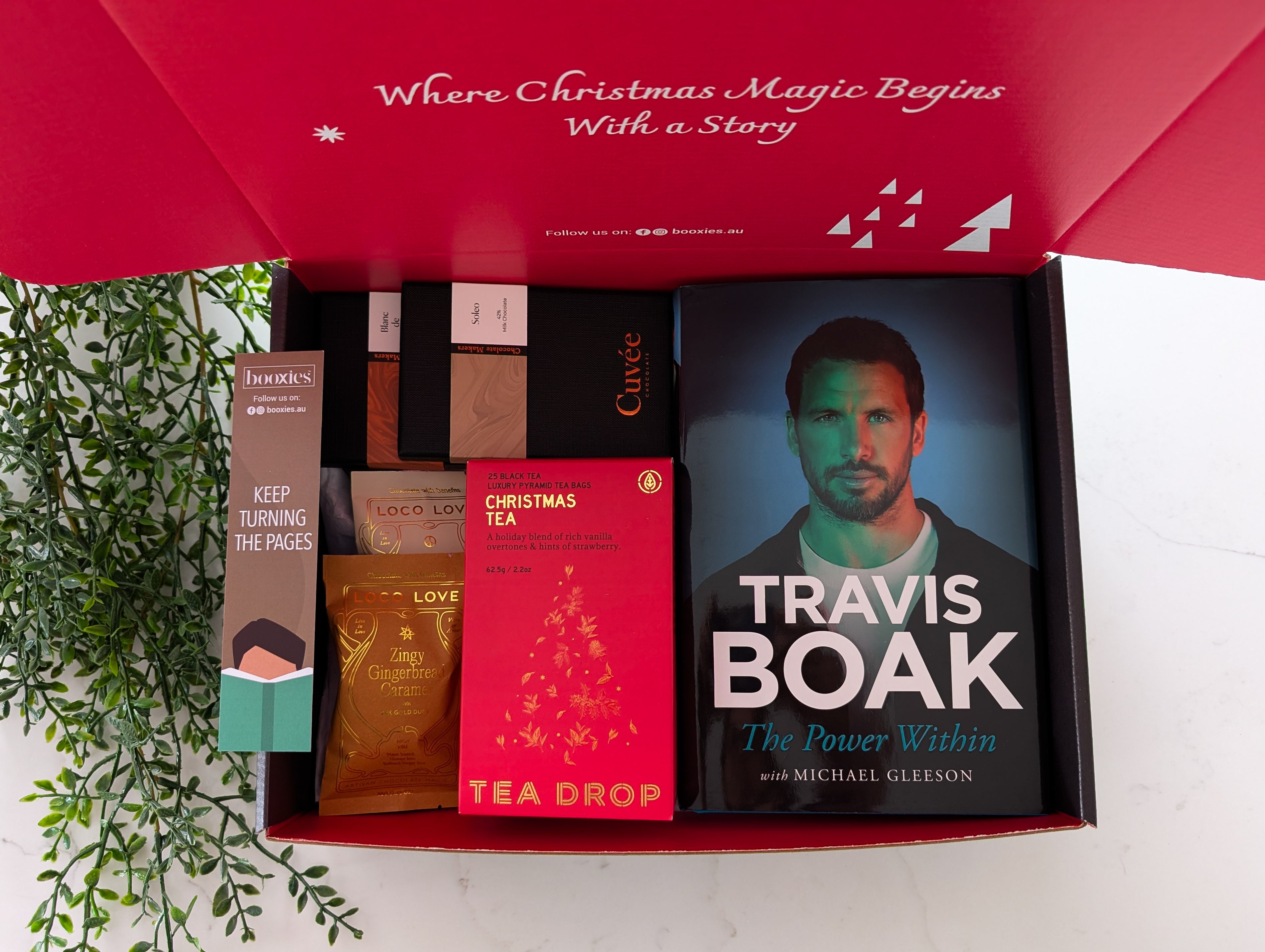 Gift set with books and tea packages on a white surface with greenery.