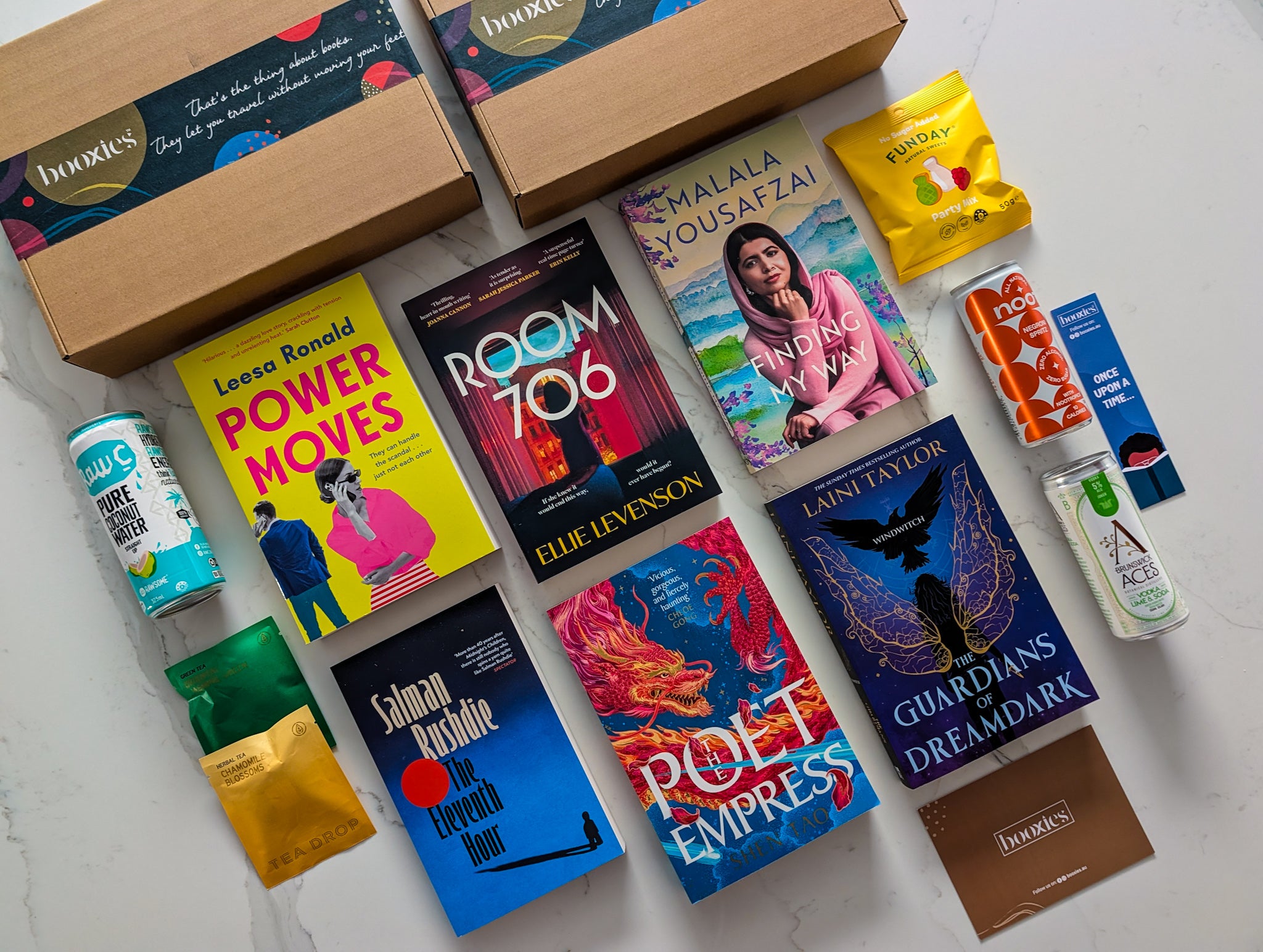 Collection of books and snacks on a white surface showing February Mystery Booxies selection