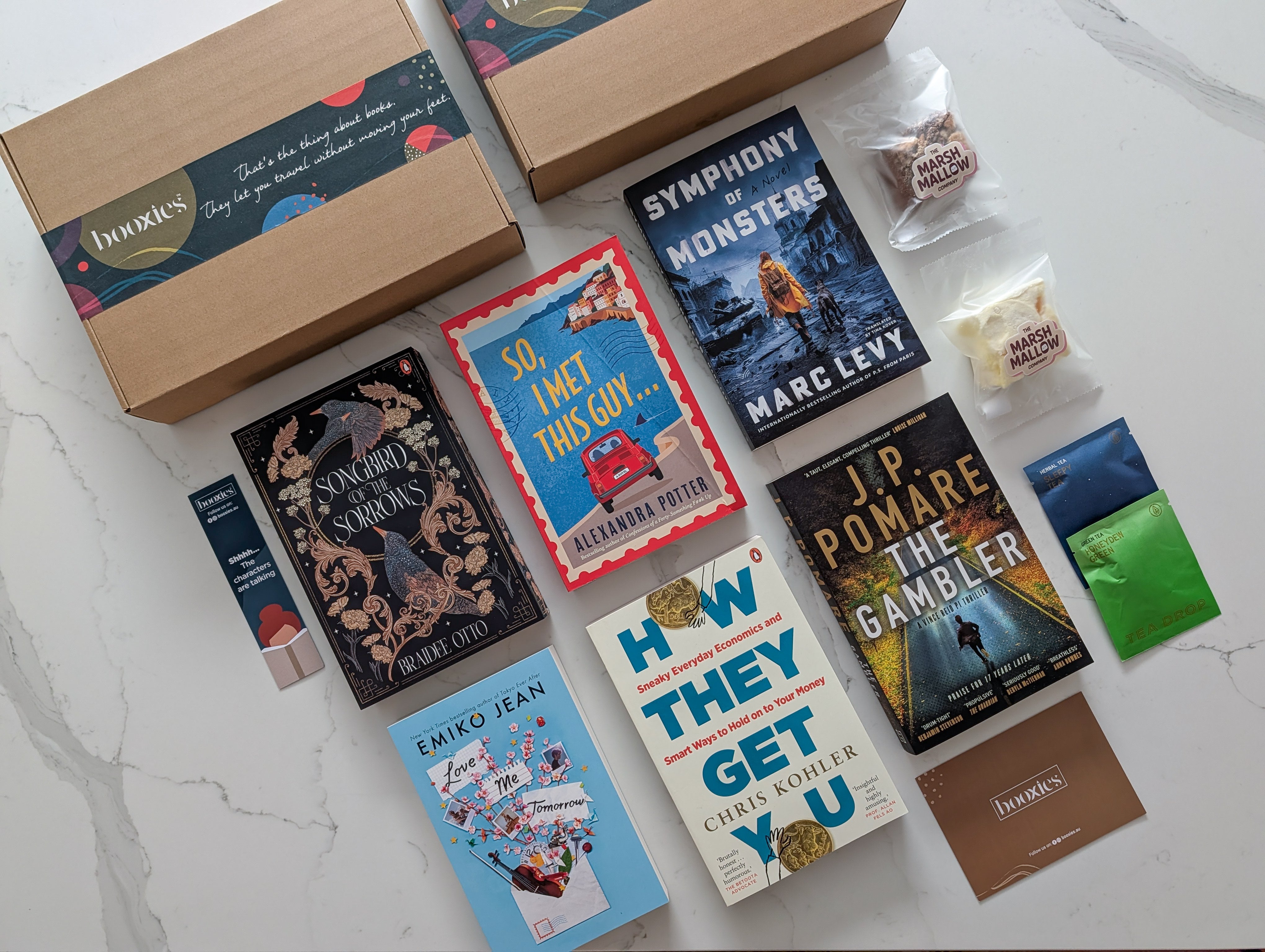 Collection of books and snacks on a white surface showing March Mystery Booxies selection