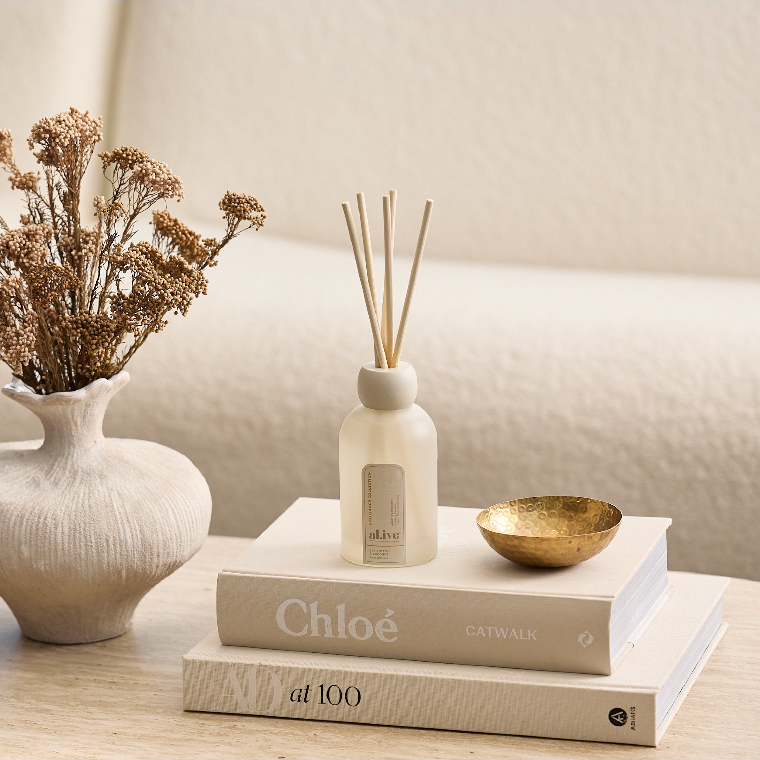 Decorative setup with books, a diffuser, and a vase on a neutral background