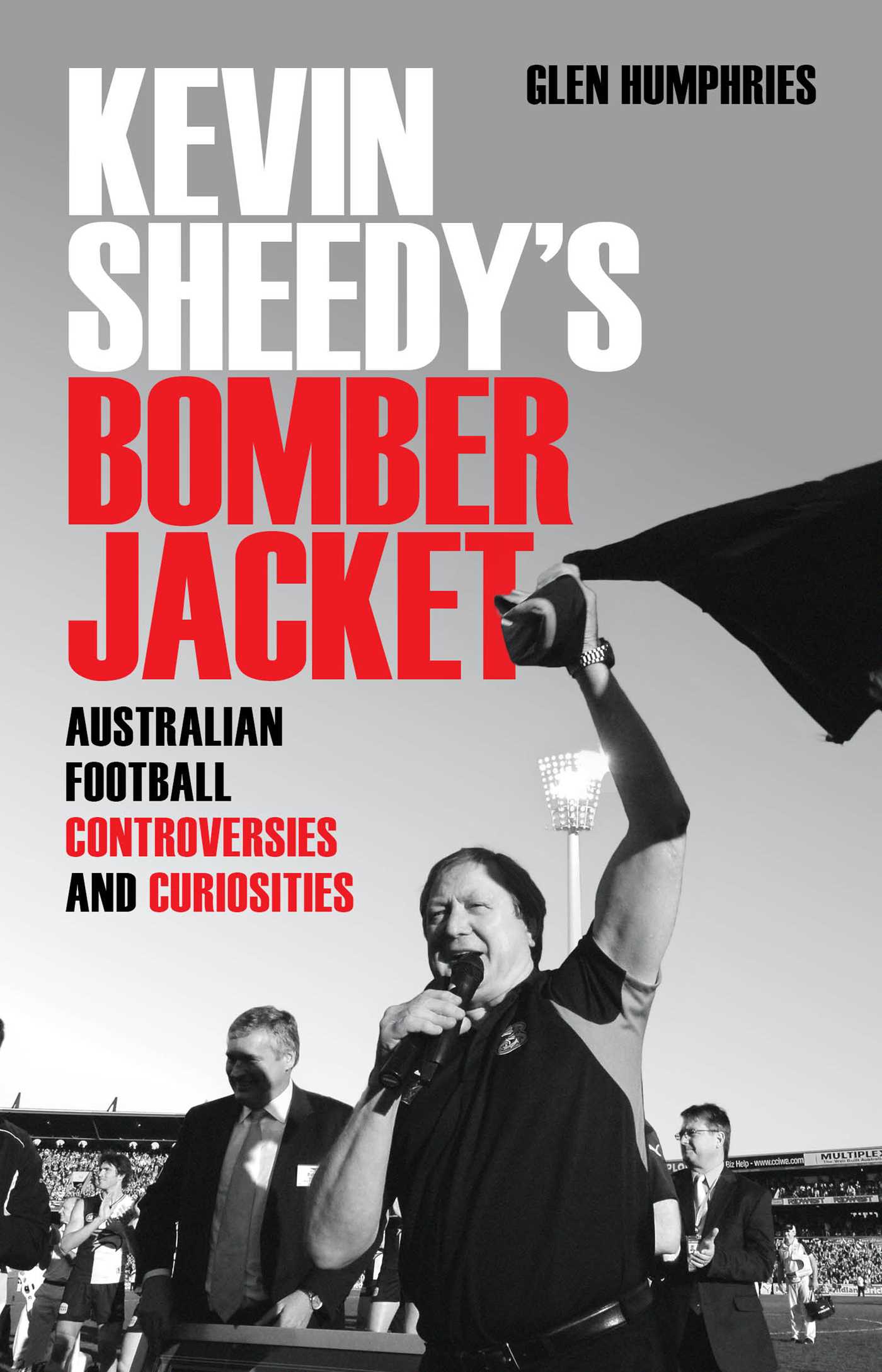 Book cover of 'Kevin Sheedy's Bomber Jacket' with a black and white photo of a man holding a microphone and a jacket.